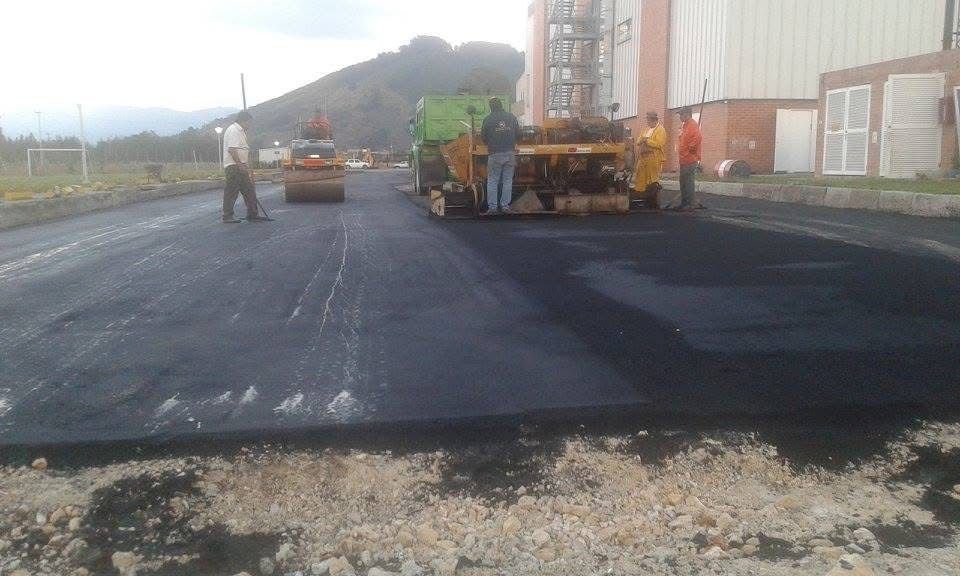 Trabajos de pavimentación con una máquina de asfalto verde y trabajadores en una carretera negra recién pavimentada 