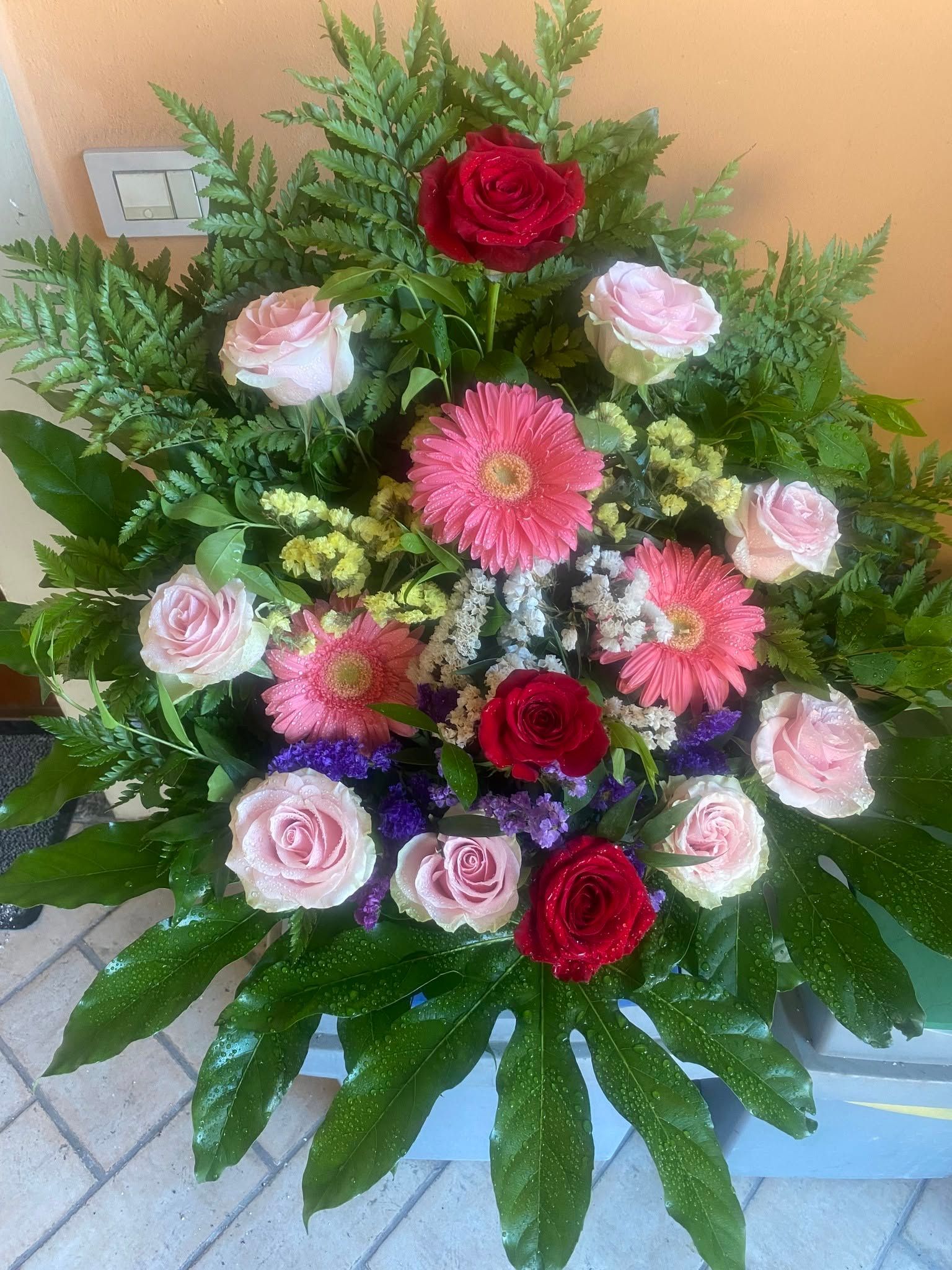 Composizione floreale mista rosa e rossa con verde in un vaso decorativo.