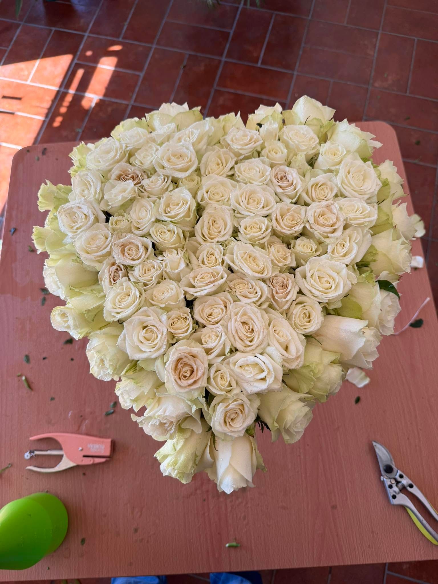 Bouquet di rose bianche a forma di cuore su un tavolo rosa, con delle forbici da potatura nelle vicinanze.