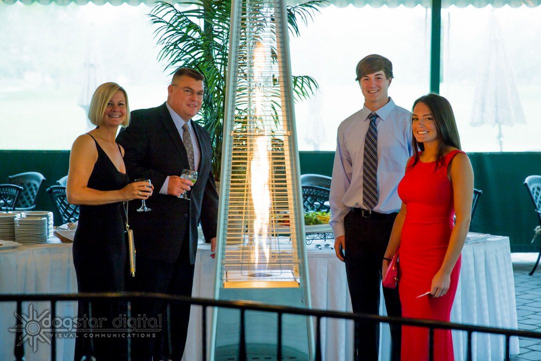 Family posing near an outdoor heater at an event. Woman in black dress, man in suit, teens in formal attire.
