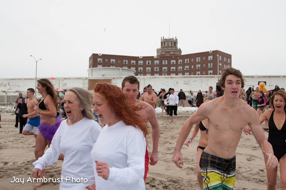 People running toward the ocean; beachfront with a brick building in the background.
