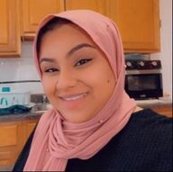 Woman in pink hijab smiling indoors, kitchen background.