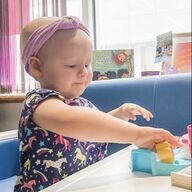 Young child in a purple headband reaching for a toy on a table.