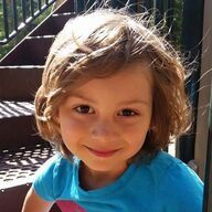 Girl with brown hair, smiling at camera, wearing blue shirt, near playground stairs.