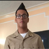 Man in military uniform and hat wearing glasses, indoors.