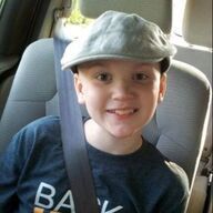 Boy wearing a cap, buckled in a car seat, smiling.