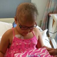 Girl in pink flamingo dress and glasses, looking down, receiving a gift in a hospital bed.