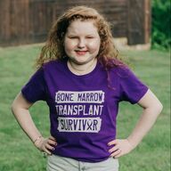 Young person with curly red hair, wearing a purple shirt that says 