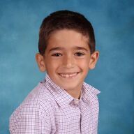 Boy with brown hair and a plaid shirt smiles in front of a blue background.