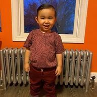 Smiling child in maroon outfit stands in front of a window and radiator.