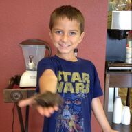 Boy in Star Wars shirt smiles, holding a dark object, indoors.