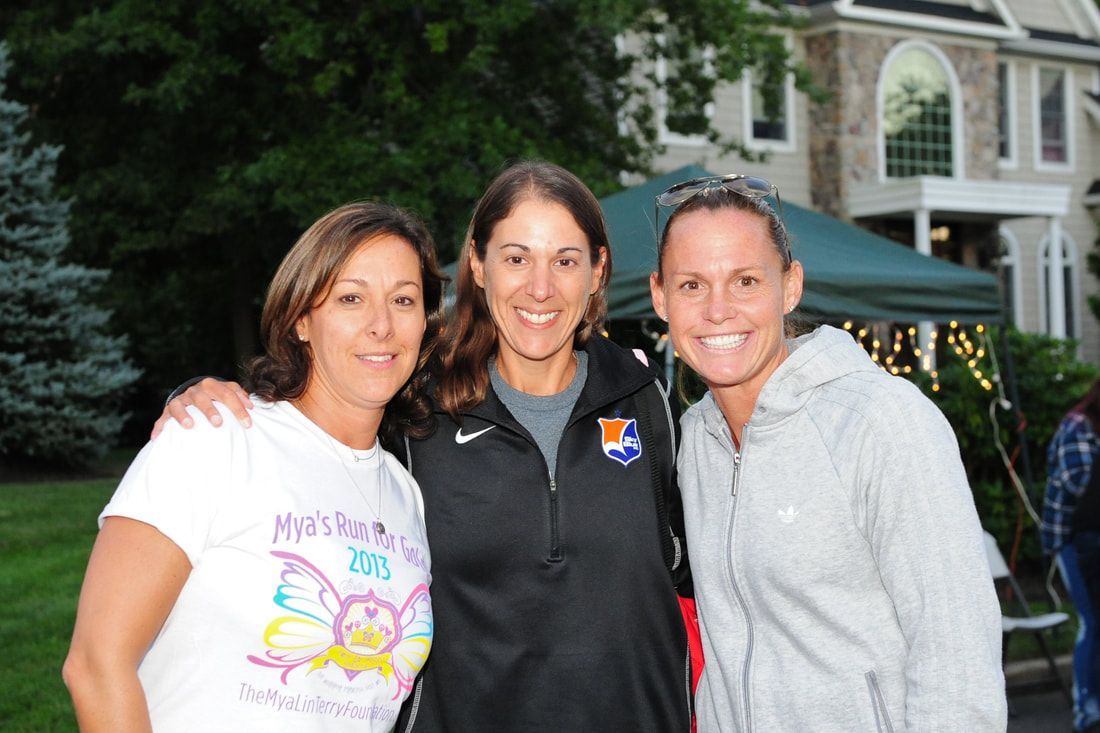 Three women smiling outdoors, posing in front of a house.
