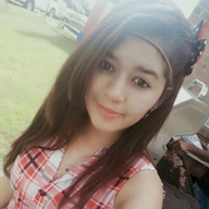 Woman with long brown hair, wearing a plaid sleeveless top, smiling outdoors.