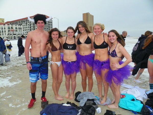 Group of people in swimwear and tutus on a snowy beach, posing.