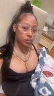 Woman in glasses holding newborn, in a hospital setting.