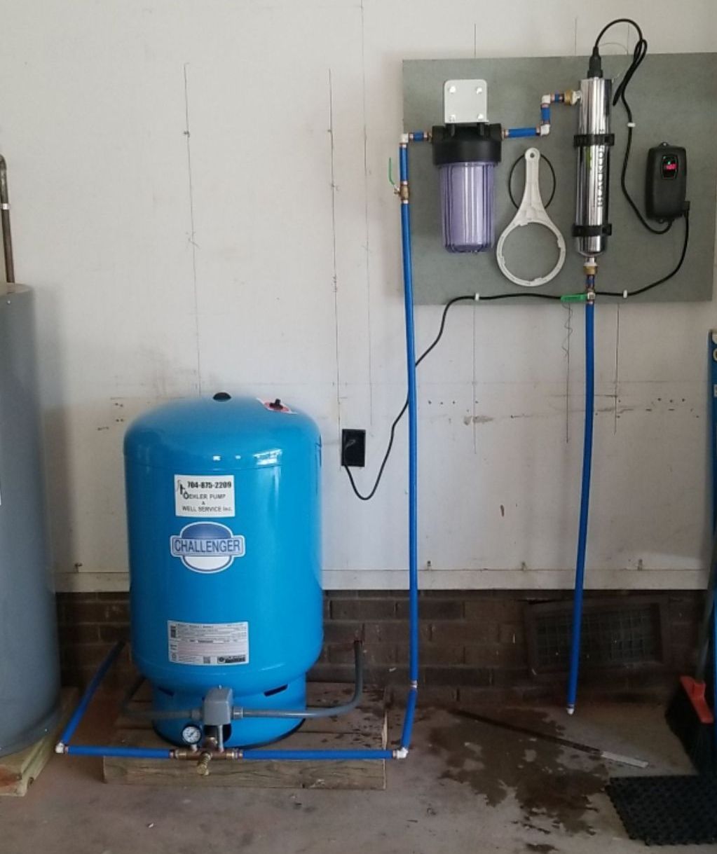 Water filtration system in a garage. Blue pressure tank, filter, and UV light on a wall.