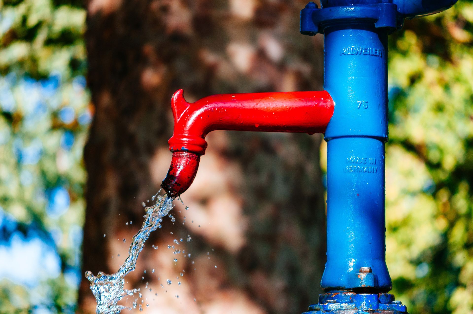 Water well pump services with a vintage red and blue outdoor hand pump with clean water stream.