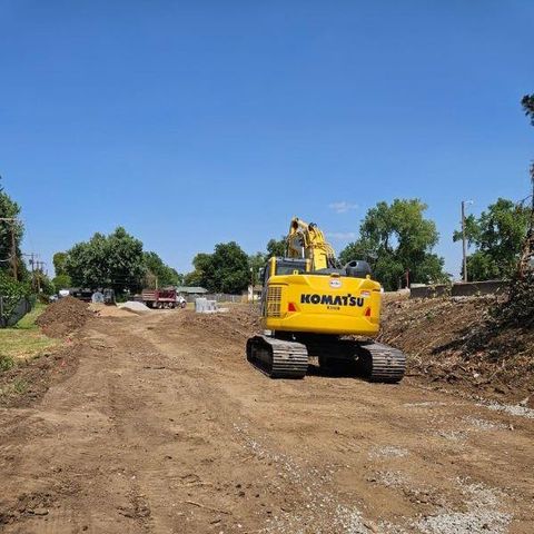 A yellow komatsu excavator is driving down a dirt road