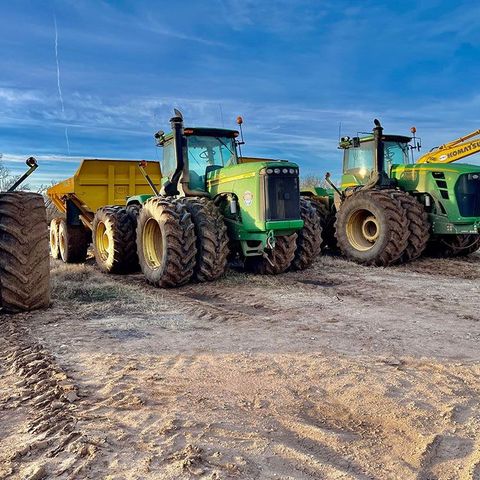 A group of tractors are parked in a dirt field.