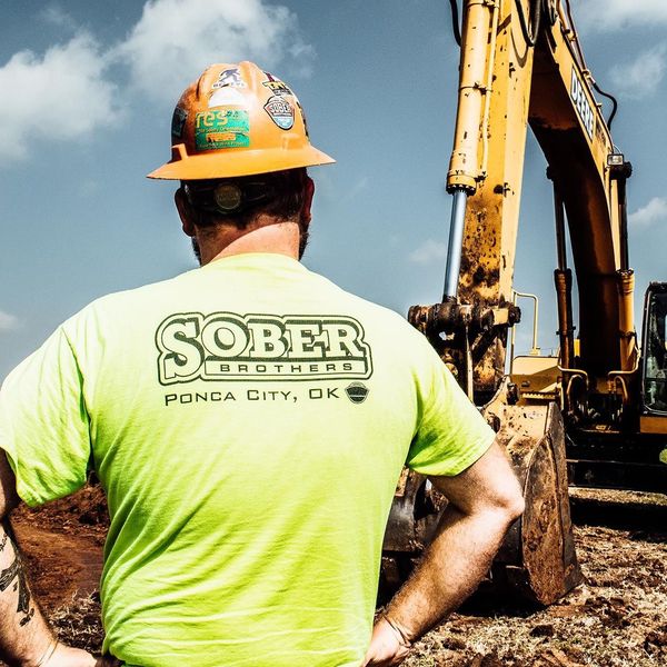 A man wearing a hard hat and a green shirt that says sober
