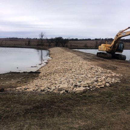 A yellow excavator is working on a dam next to a lake.