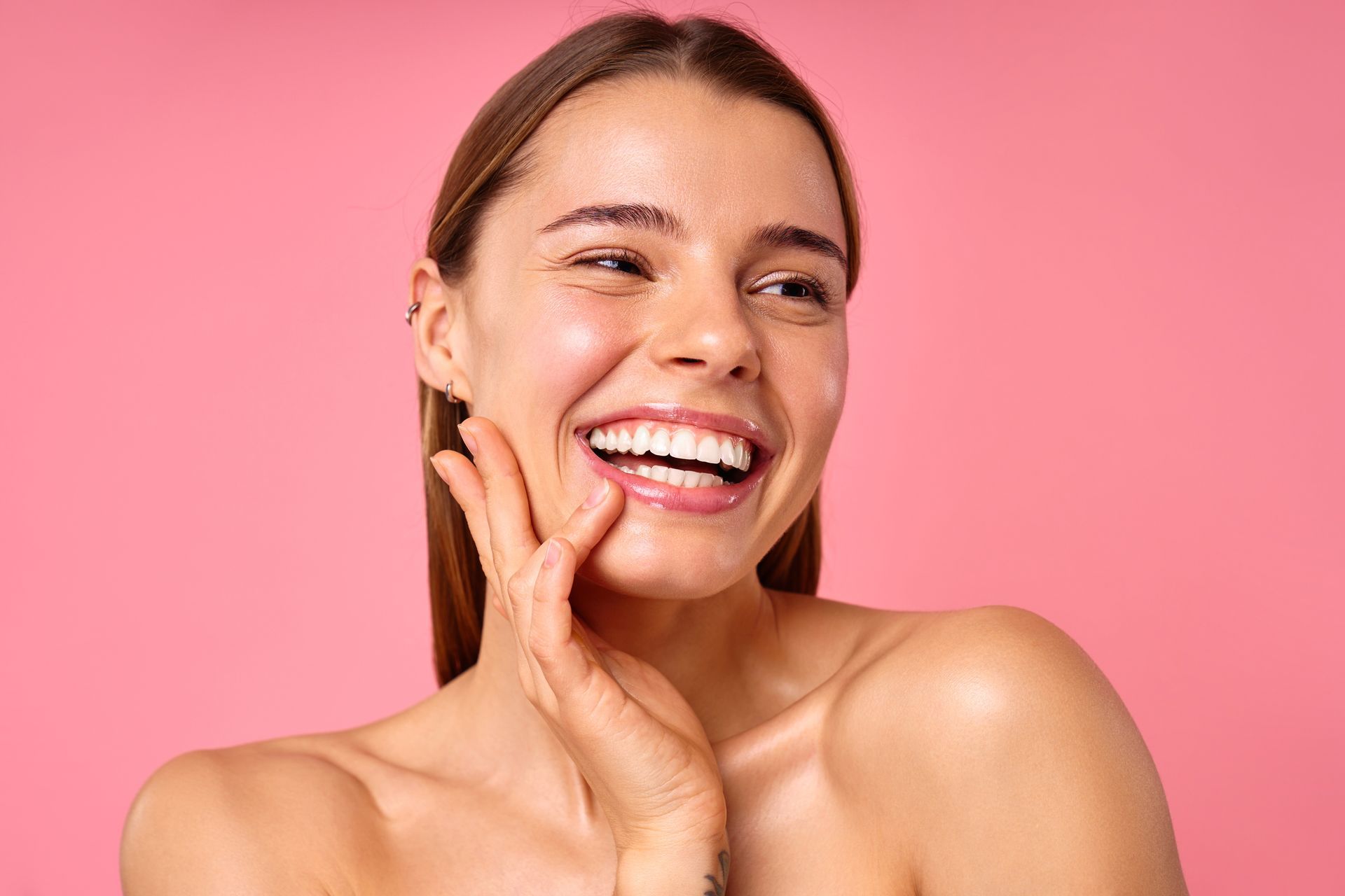 Smiling person touching their cheek against a pink background