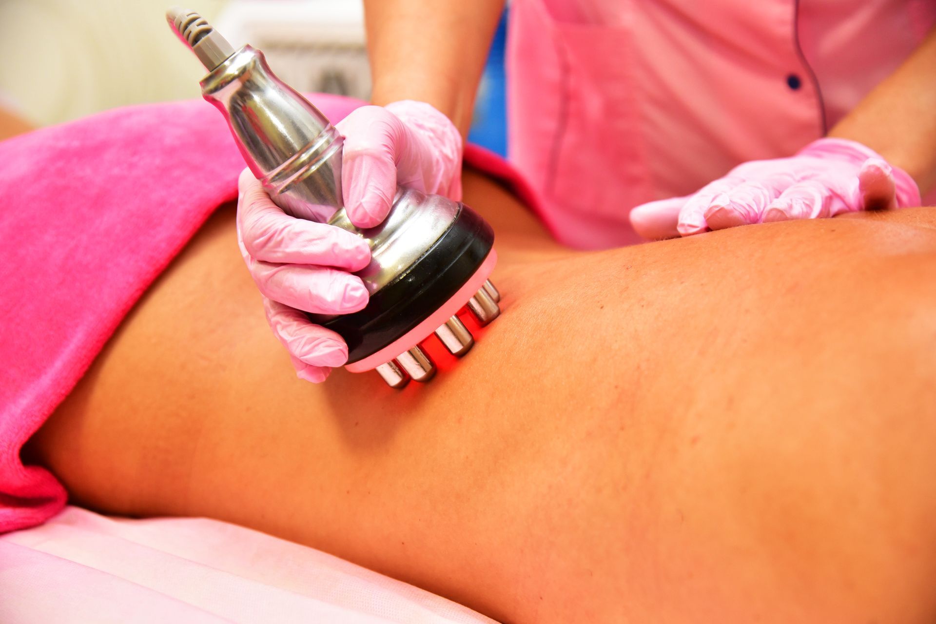 Person using a handheld massage device on a client’s bare back in a spa setting