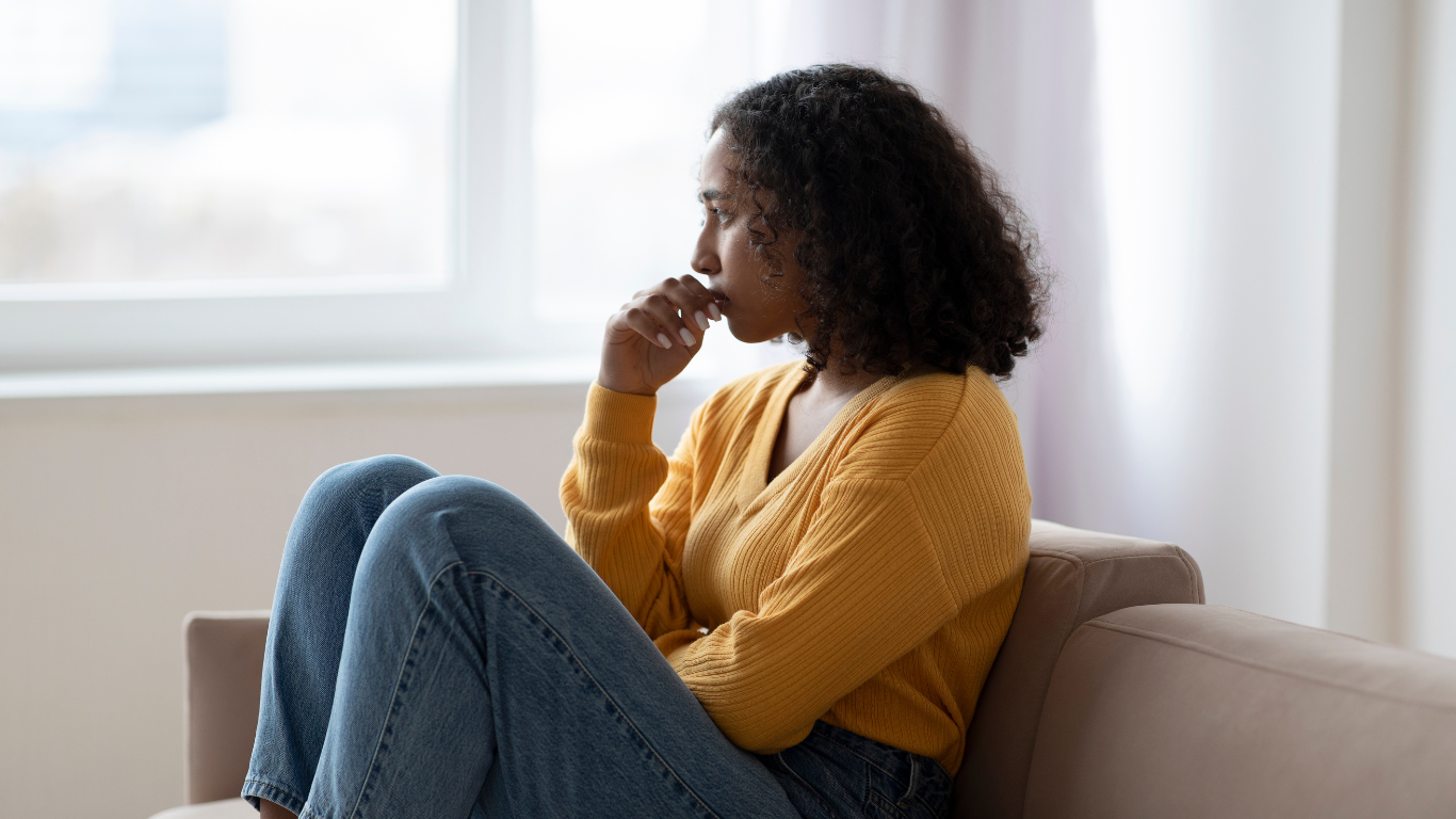 Person in hoodie sits on couch, facing a person in a chair. Counseling session in a room.