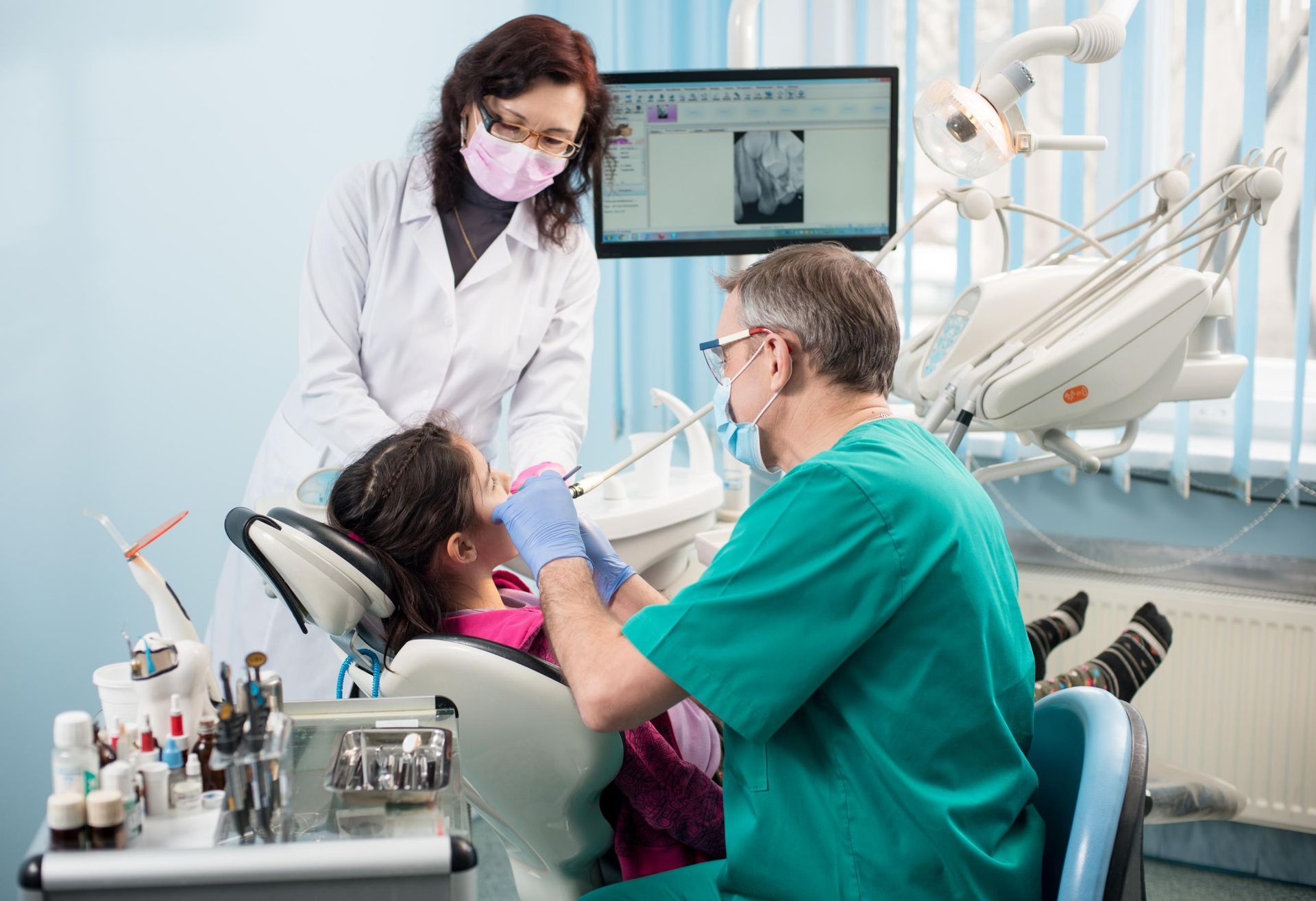 A dentist and an assistant perform a procedure on a patient in a clinical office setting.