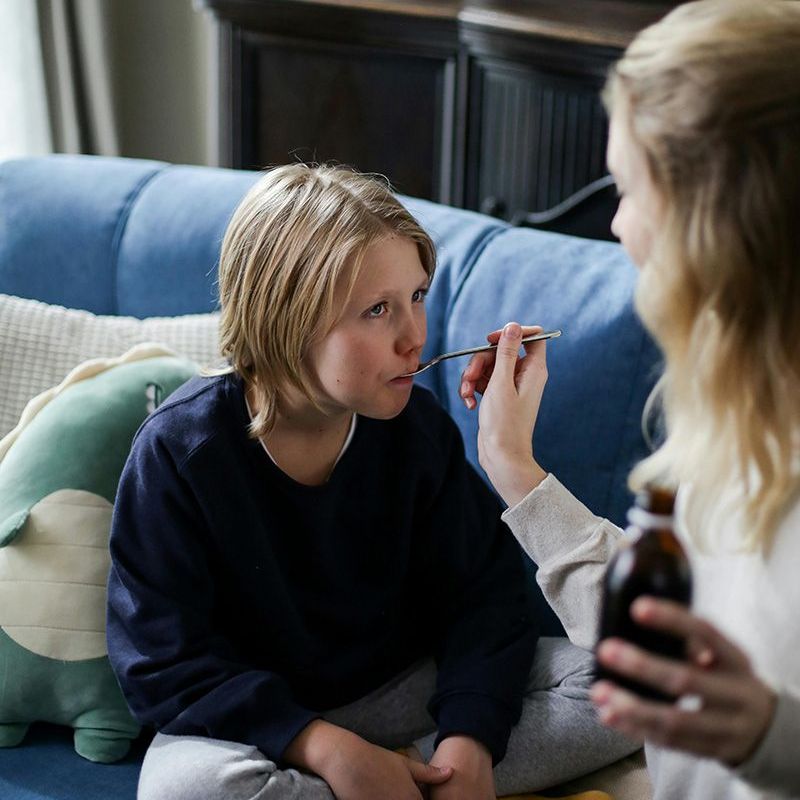 Person getting their face painted on a blue couch while another holds a paintbrush and bottle