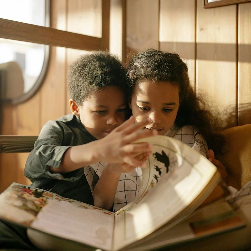 Two children reading a picture book together in a sunlit wooden room
