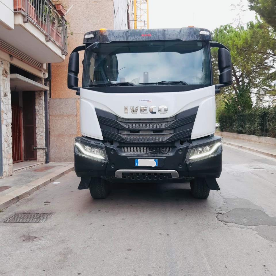 Un camion IVECO bianco parcheggiato in una strada stretta. Il camion è rivolto verso la telecamera.
