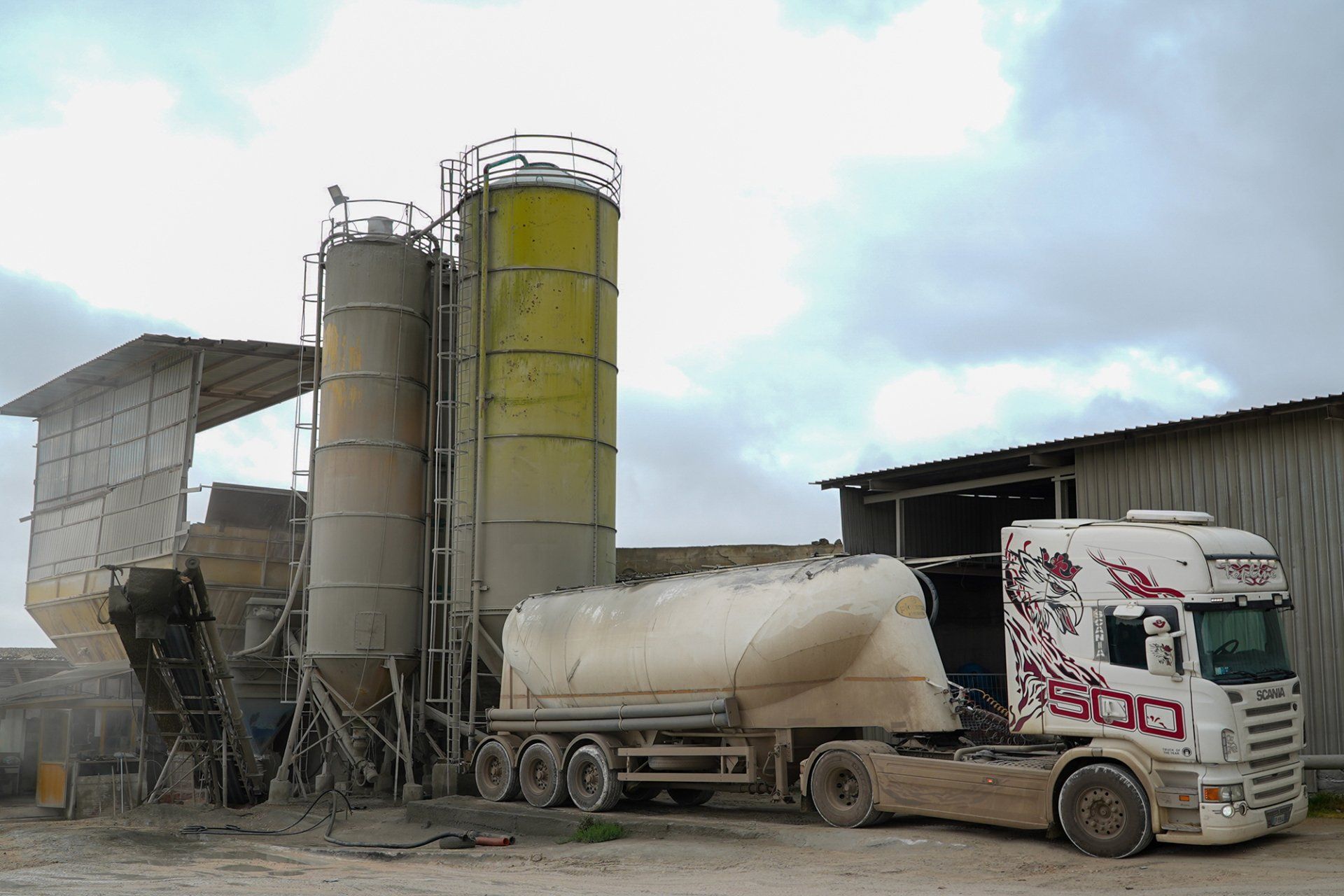 Impianto di betonaggio con silos, camion e area di carico sotto un cielo nuvoloso.