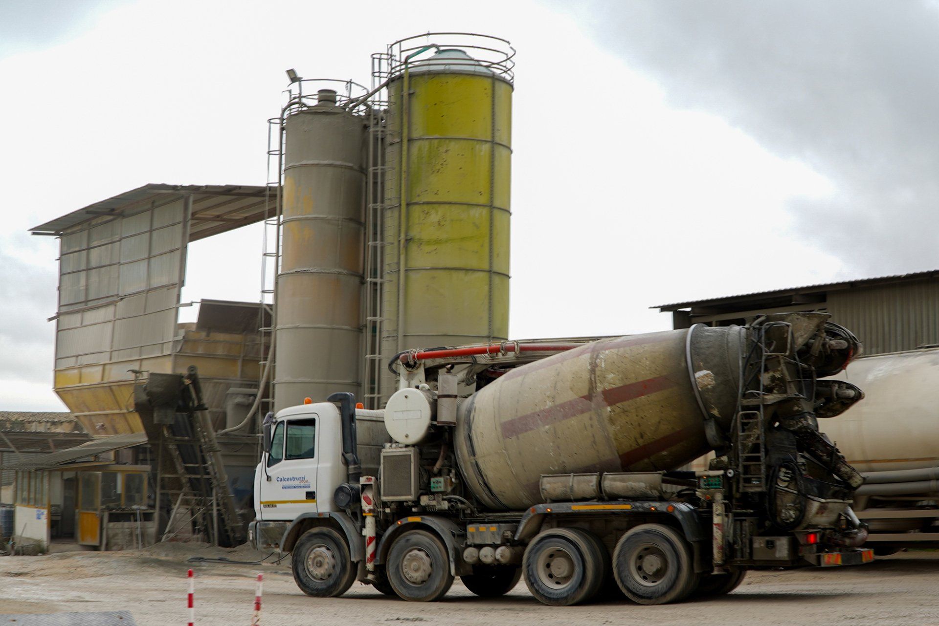 Autobetoniera davanti a un impianto di betonaggio con silos e altre attrezzature.