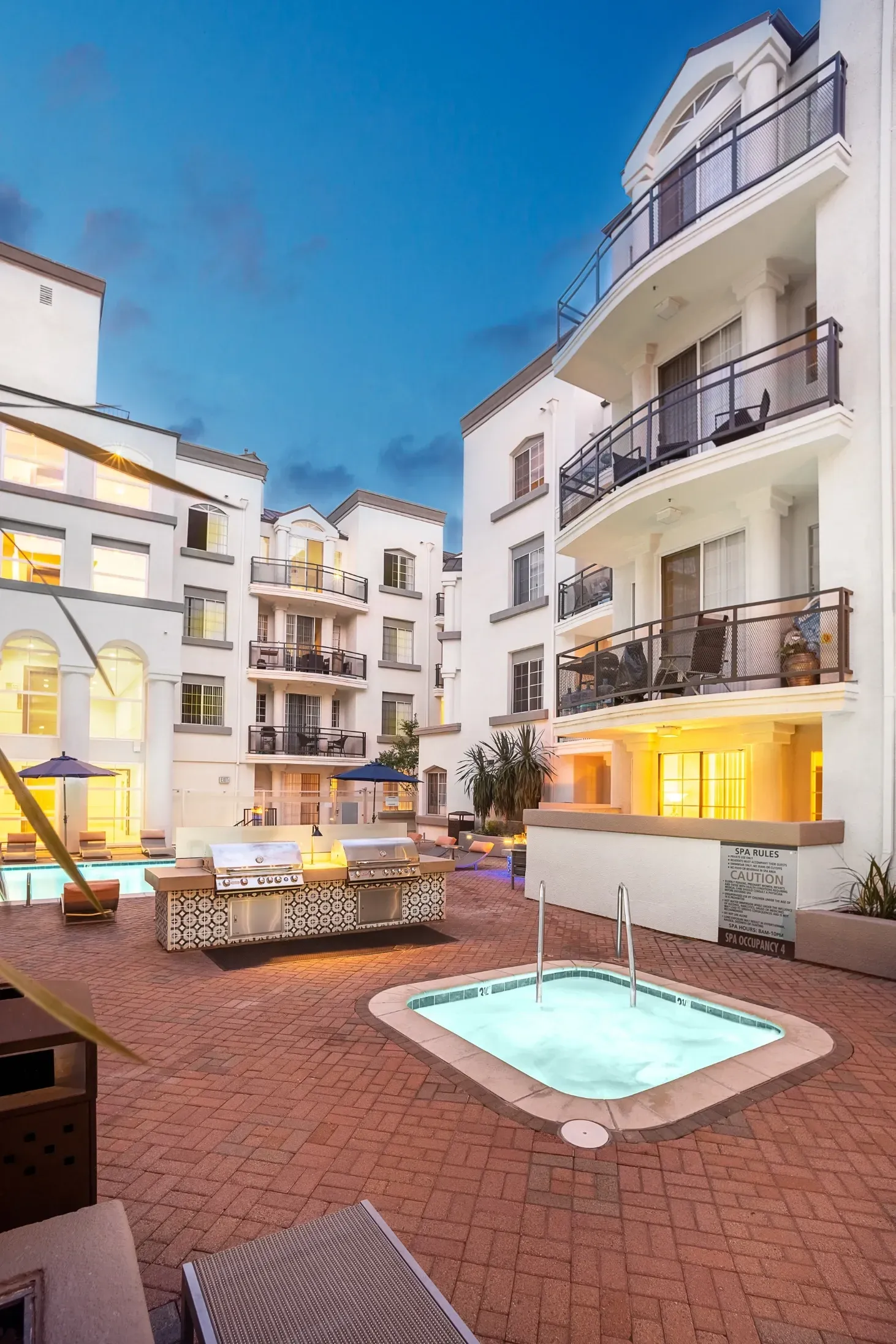 Outdoor hot tub and grilling area next to a pool at a multifamily property.