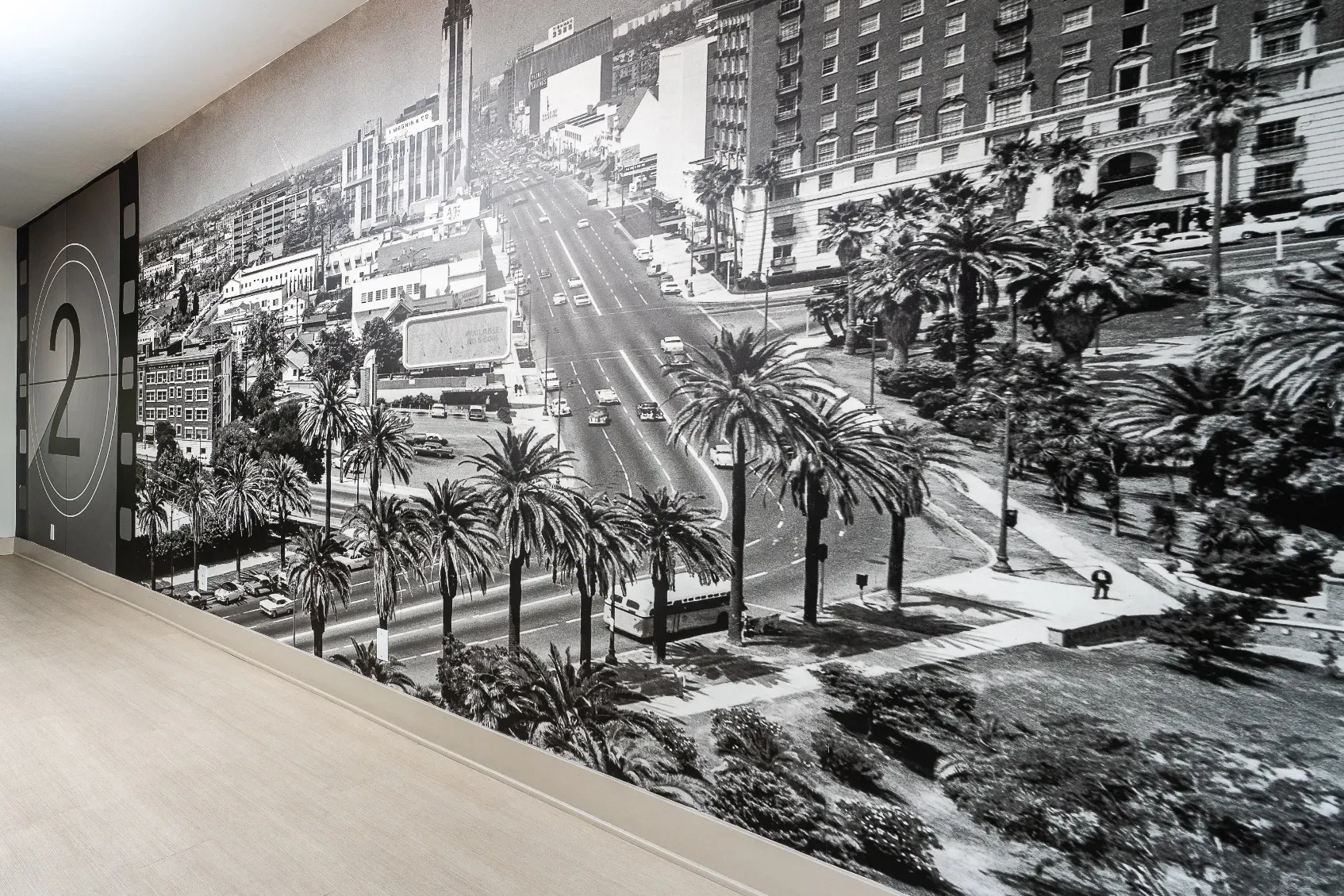 Black and white mural of a city street with palm trees and cars.