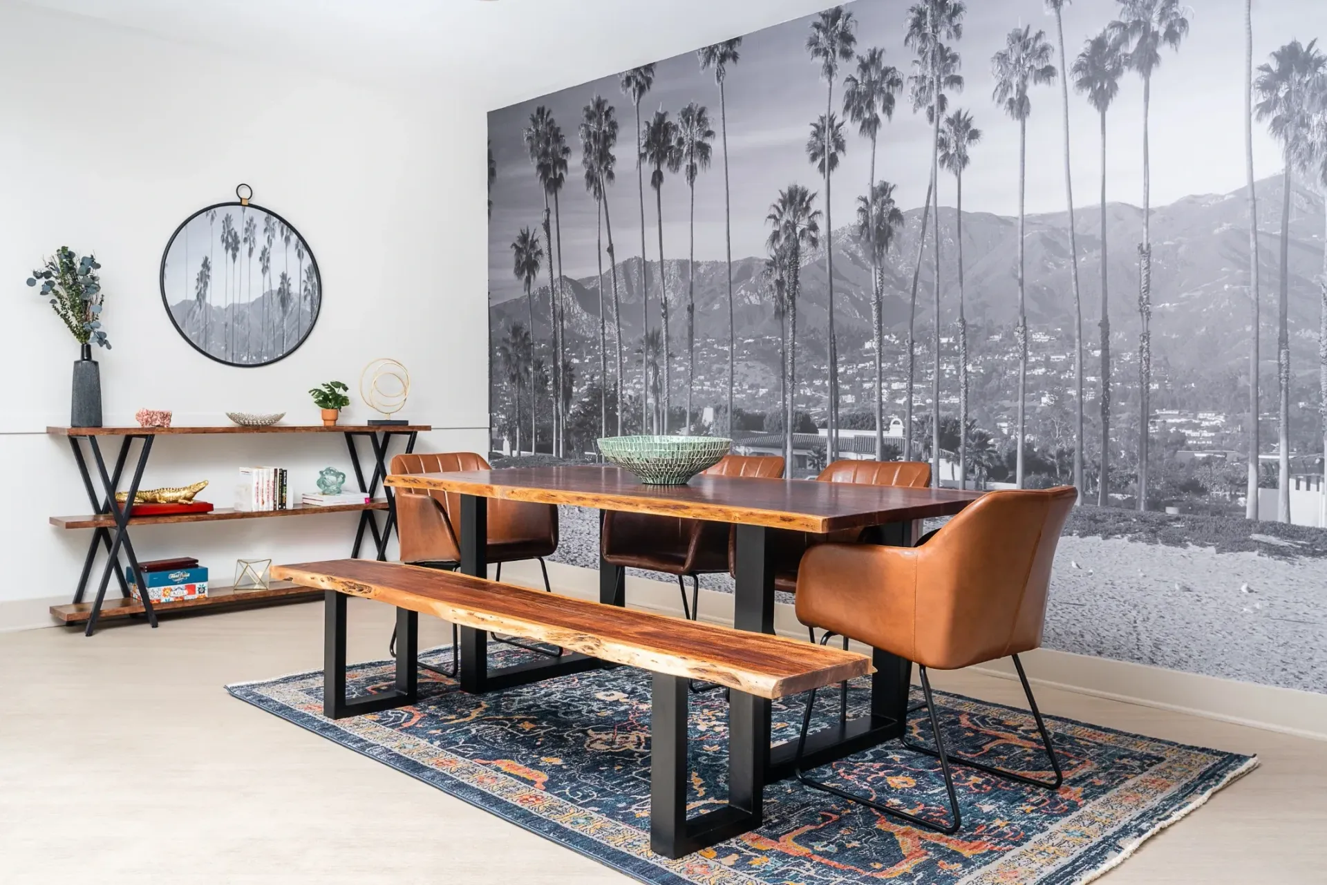 Dining area with live-edge table and leather chairs against a scenic mountain and palm tree mural.
