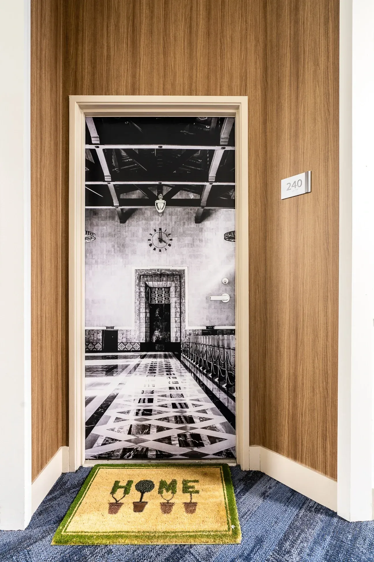 Doorway to apartment 240, featuring a black and white mural of an ornate building interior and a 'HOME' doormat.