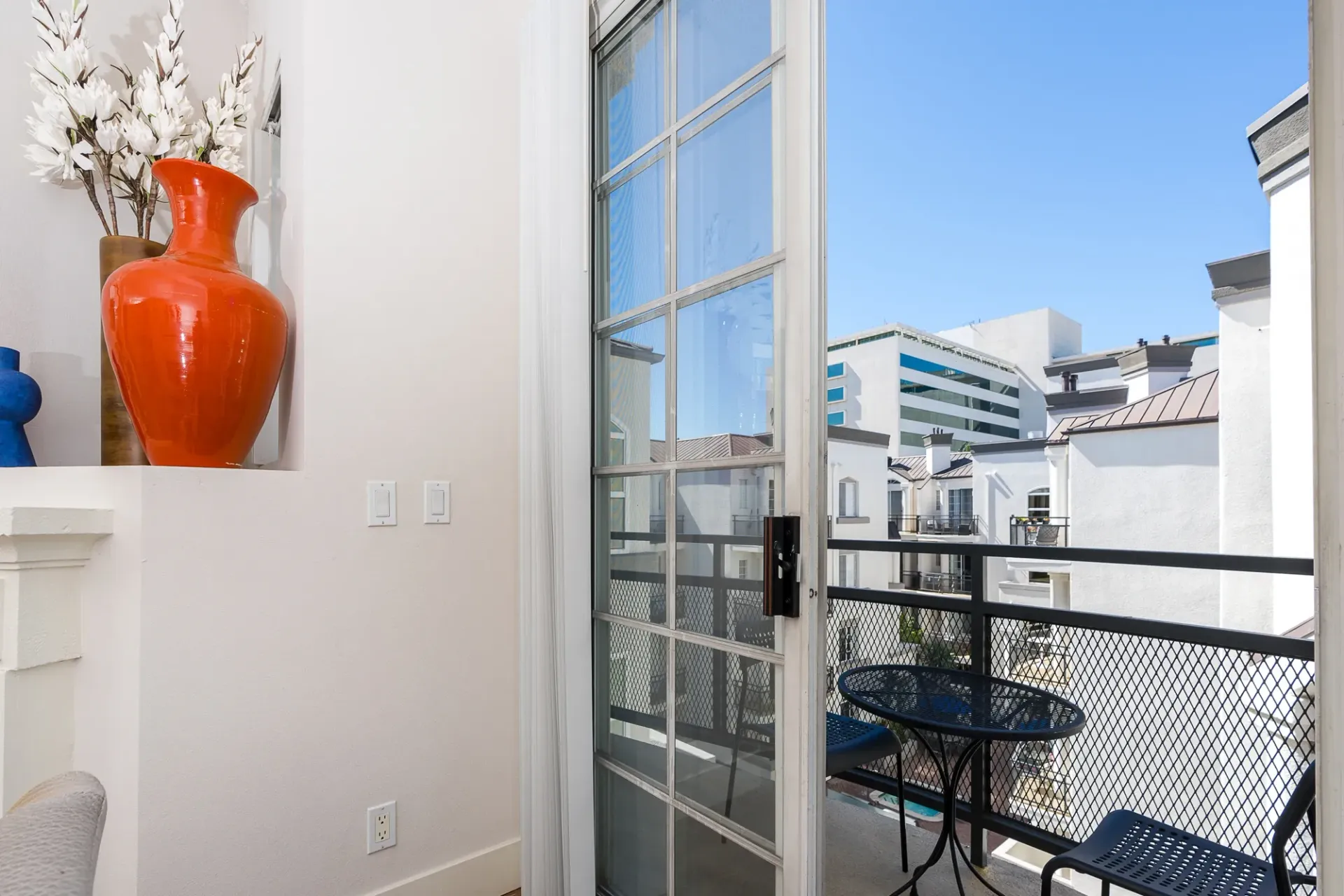Balcony view from apartment overlooking buildings and a courtyard with a table and chairs.