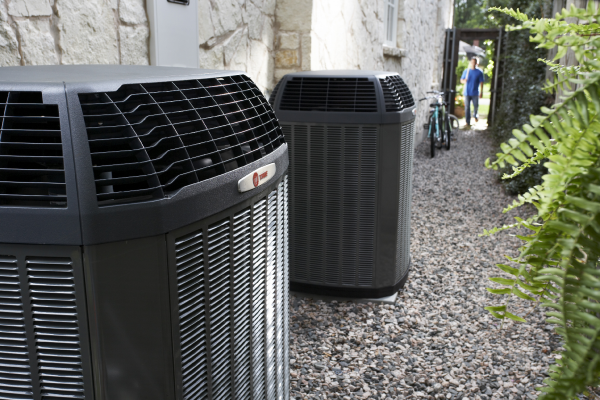 Two outdoor air conditioners beside a gravel path, with a person in the background near a gate