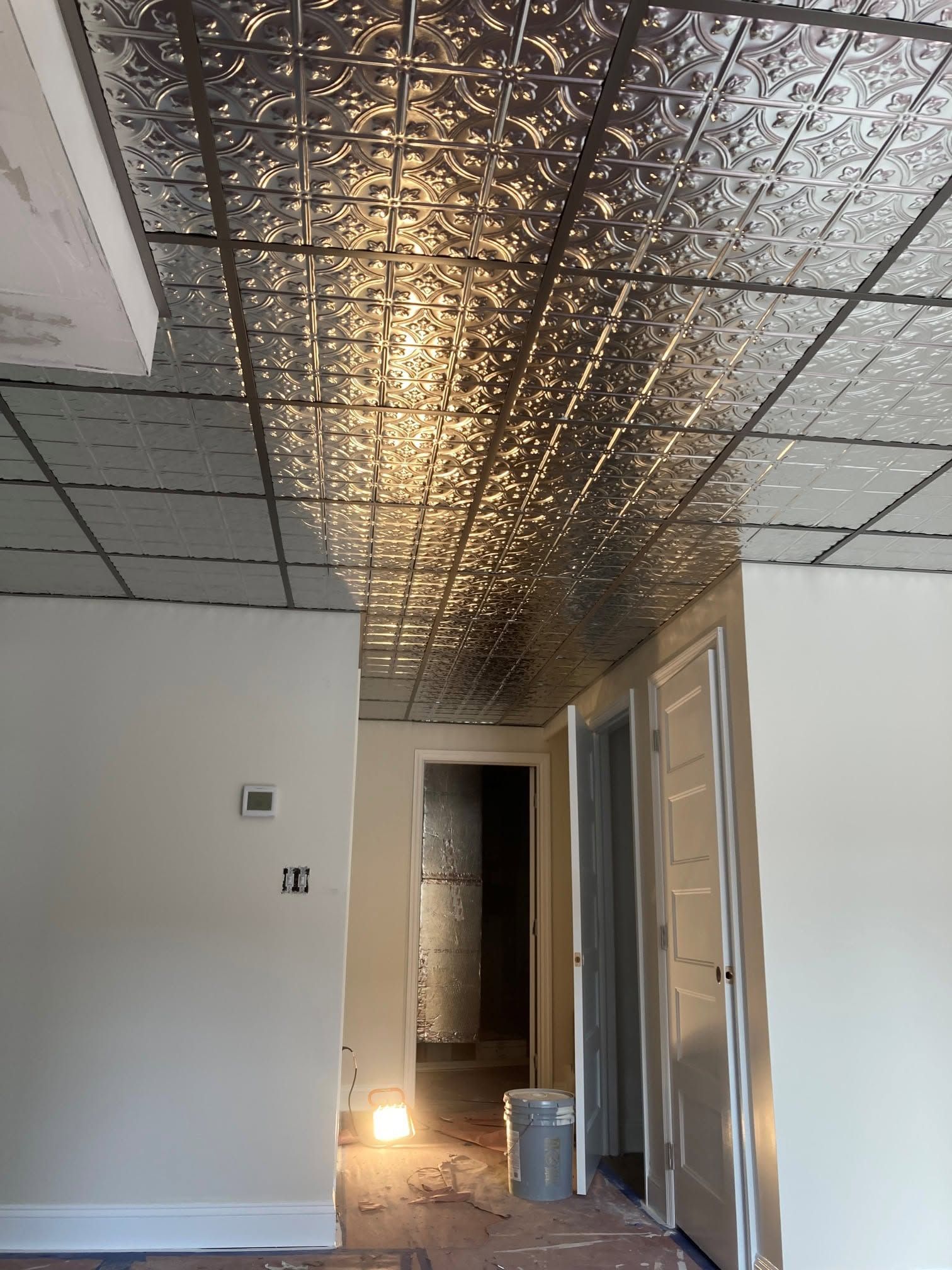 Empty room with white walls, a reflective ceiling, and a lit doorway in the hallway beyond.