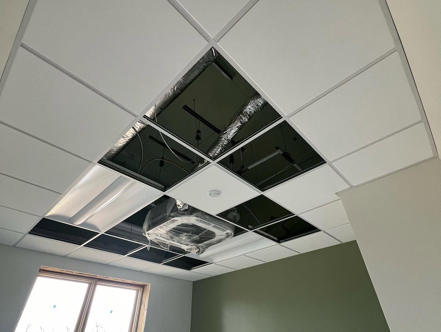 Damaged ceiling with missing tiles and exposed ductwork in a room with green walls and a window.