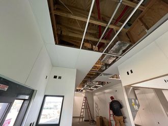 Interior under construction with exposed ceiling beams, ladders, and two workers in a hallway