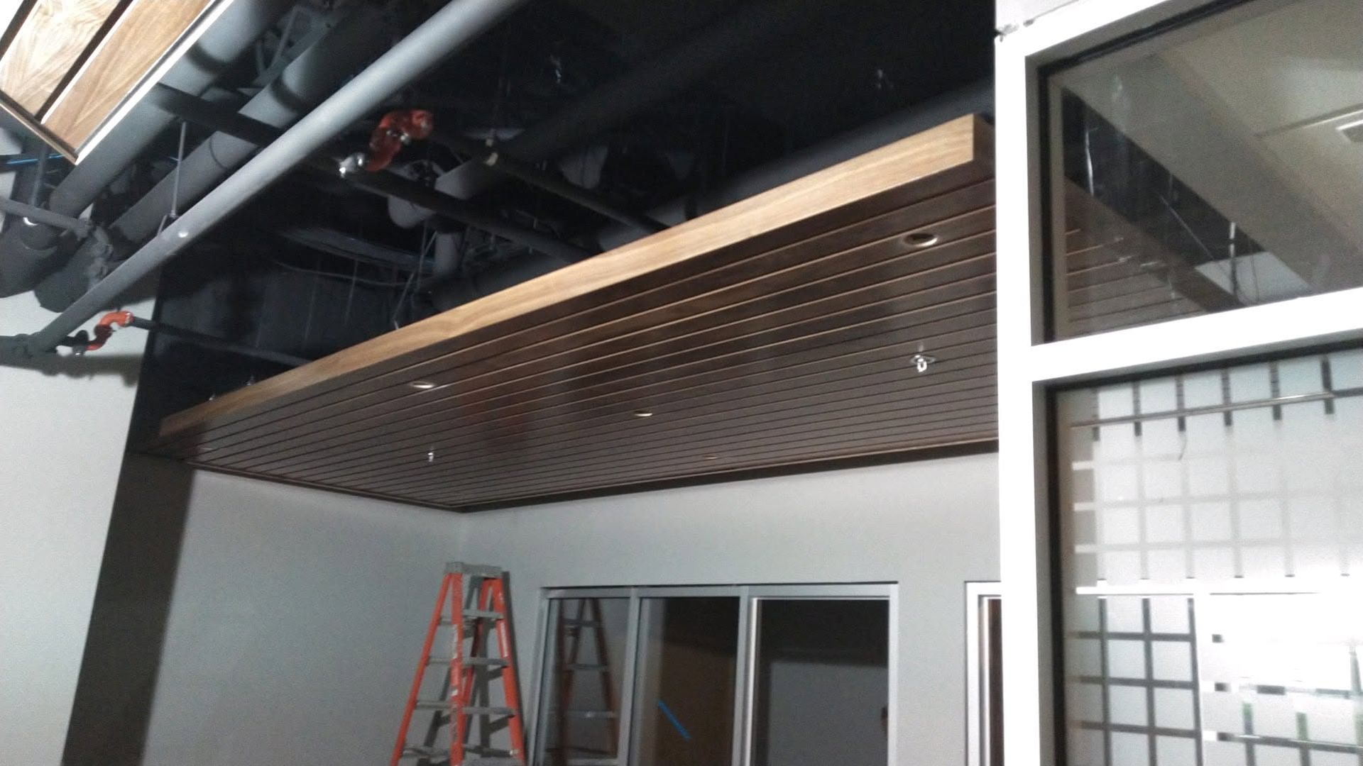 Partially finished interior with exposed beams, wood slat ceiling, ladder, and glass doors