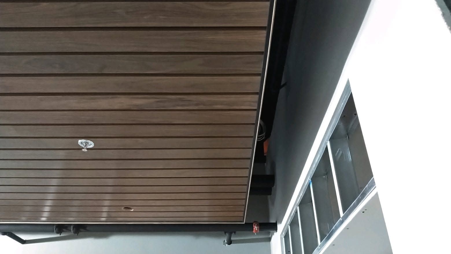 Ceiling with dark wooden slats and a white wall with windows along the side.