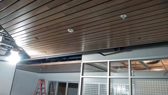 Ceiling under repair with exposed beams, a ladder, and glass wall panels in an indoor space