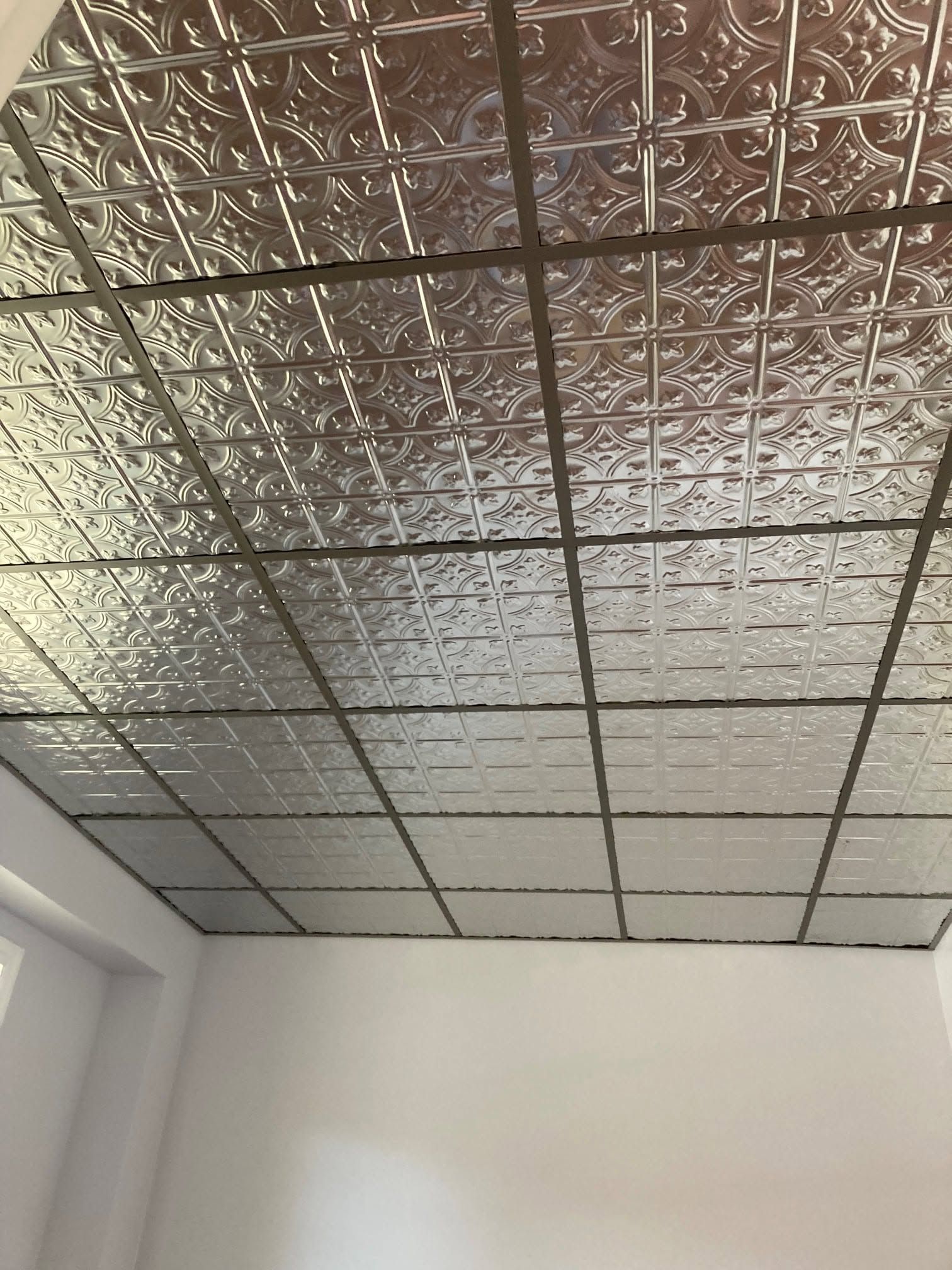 White ceiling with reflective foil tiles and a metal grid above plain white walls