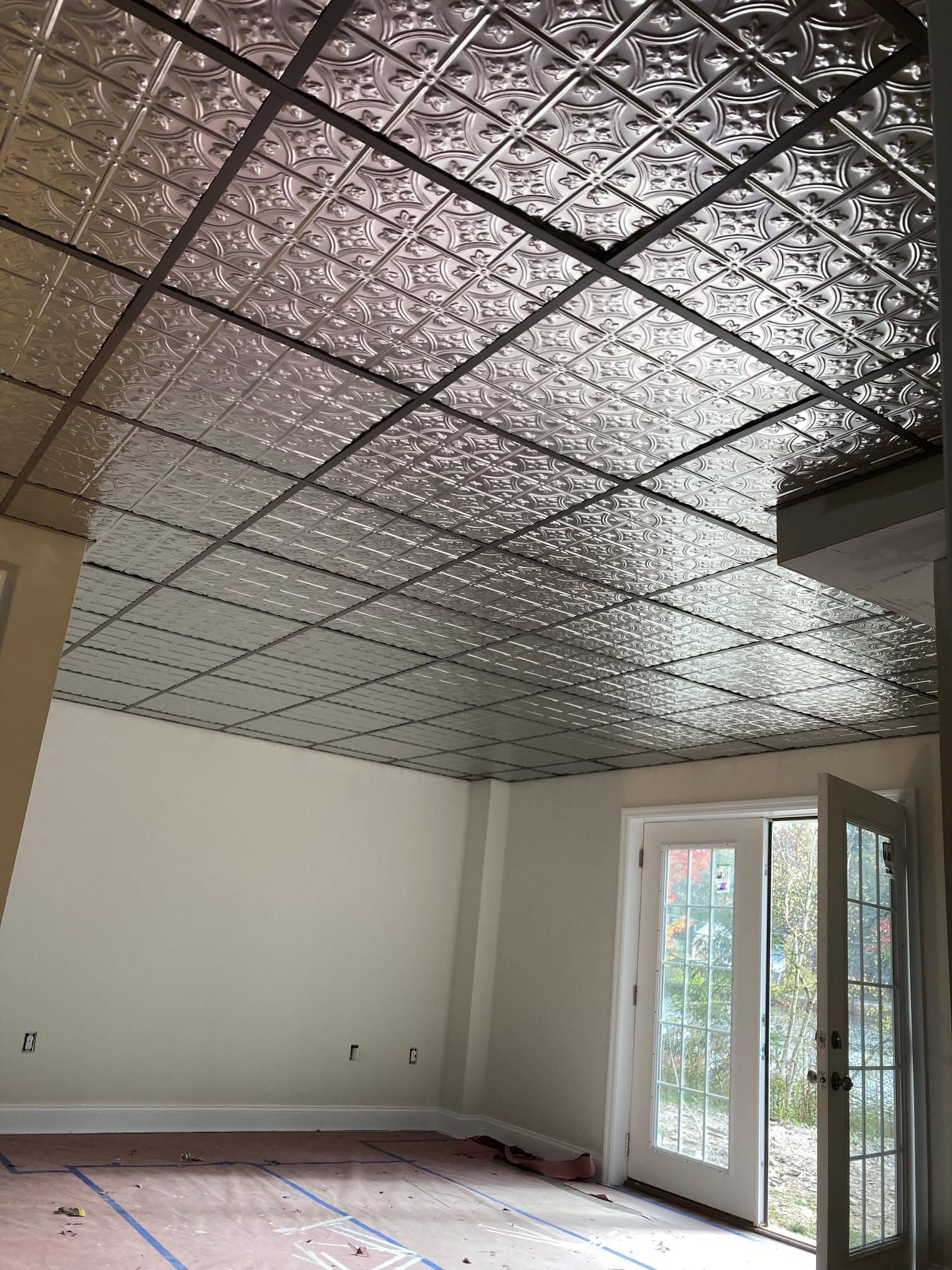 Empty room with tiled drop ceiling, white walls, and French doors opening to a garden.