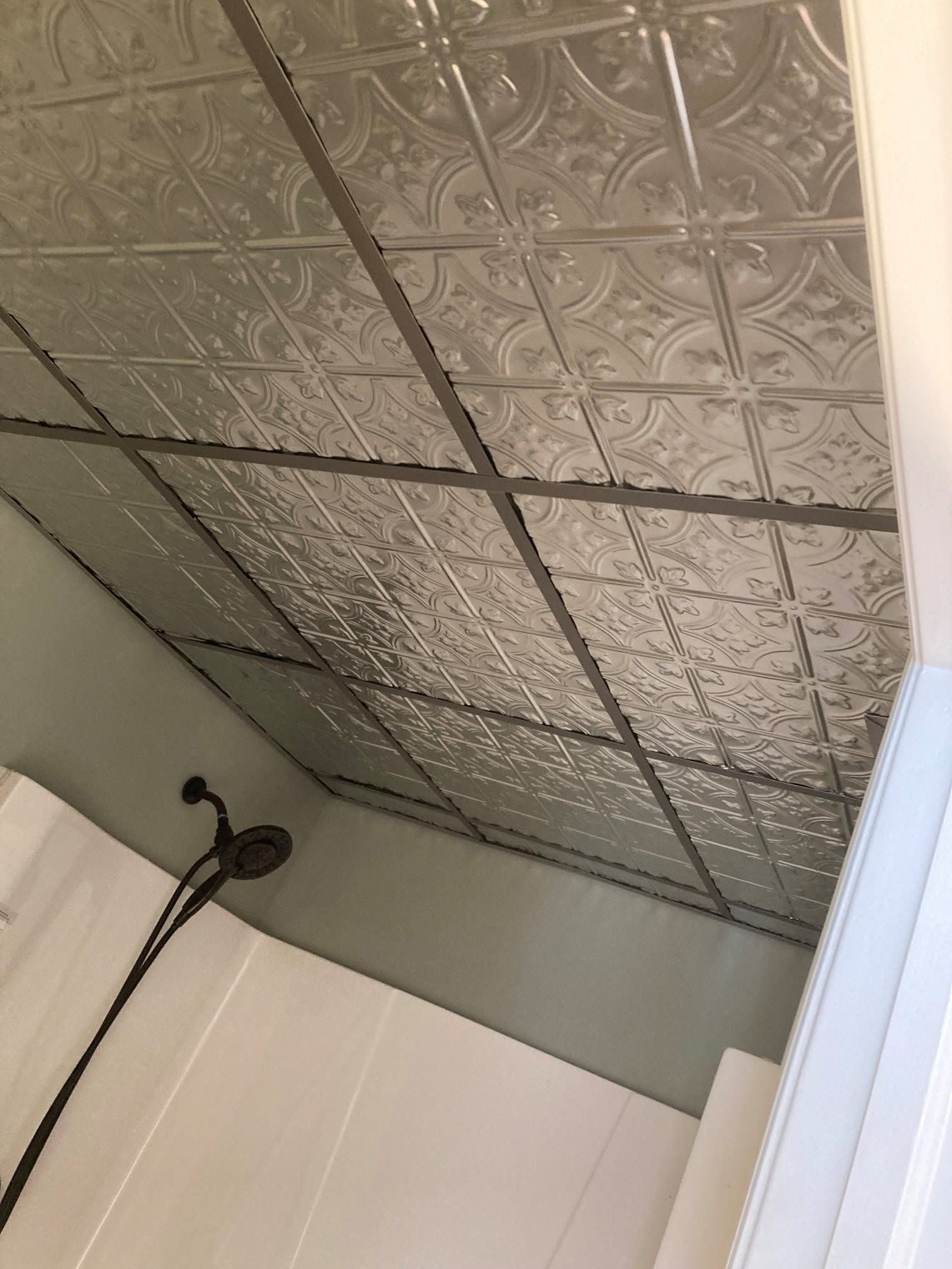 Corner of a room with a patterned metal ceiling, wall junction, and hanging black cable.