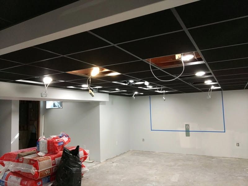 Unfinished basement room with exposed ceiling lights, gray walls, and stacked supplies on the left.
